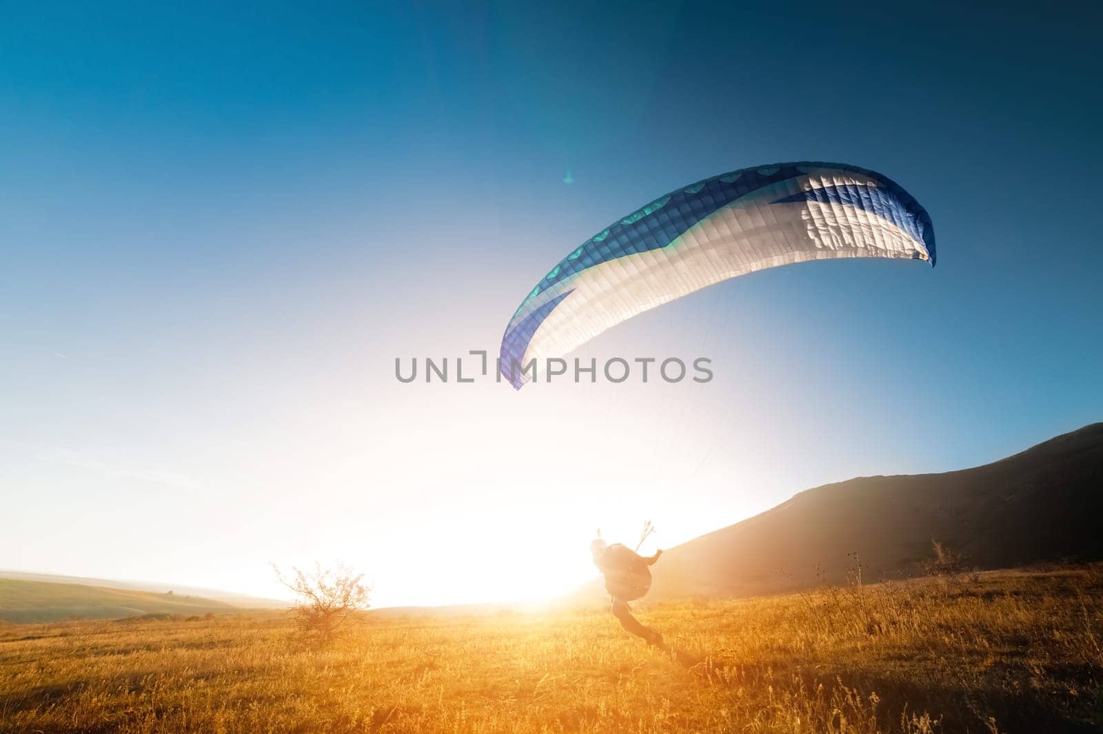 Launching a speedwing from a mountain. A paraglider is preparing to take off from a mountain, running along the yellow autumn grass against the sun.
