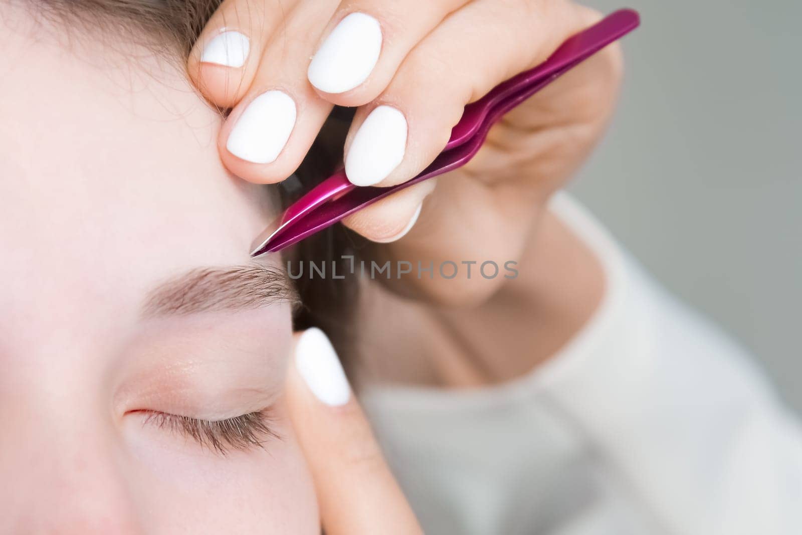 A makeup artist plucks a young woman's eyebrows with tweezers. Beautiful thick eyebrows close-up. Professional makeup and cosmetological skin care in a beauty salon