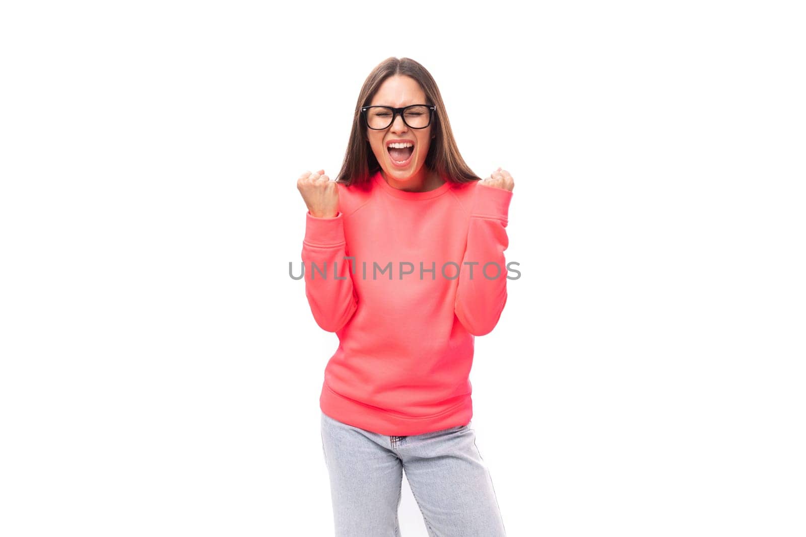 pretty joyful young brunette caucasian woman with straight hair is dressed in a pink sweatshirt and jeans on a white background with copy space.