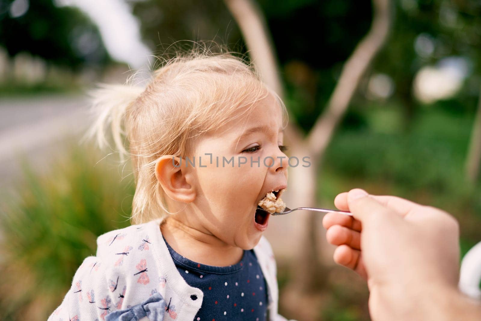 Dad feeds porridge from a spoon to a little girl. High quality photo