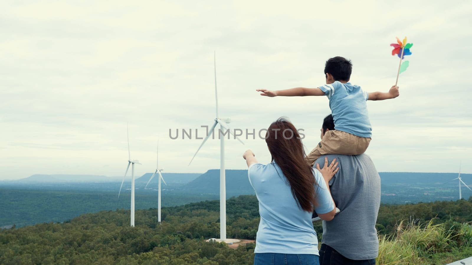 Concept of progressive happy family enjoying their time at the wind turbine farm. Electric generator from wind by wind turbine generator on the country side with hill and mountain on the horizon.
