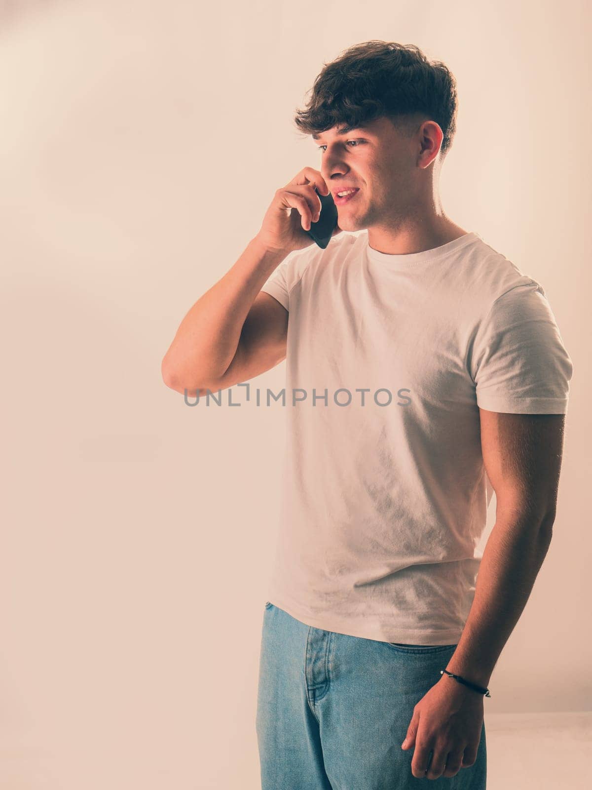 Handsome Young Man in a White Shirt Engaged in a Phone Conversation by artofphoto