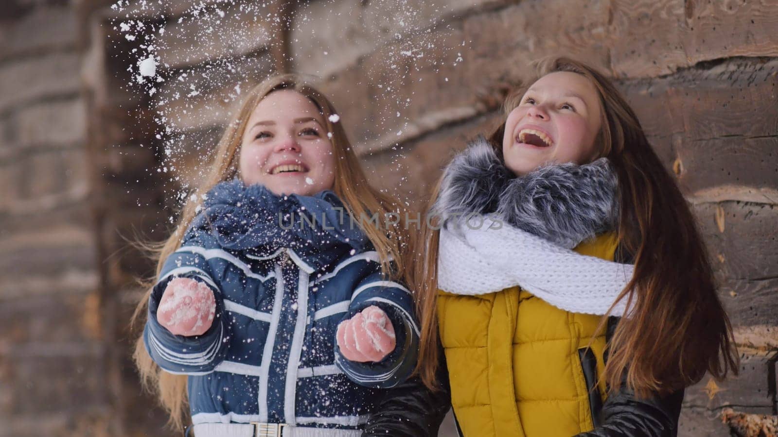 Two girlfriends toss snow in the winter in the village. by DovidPro