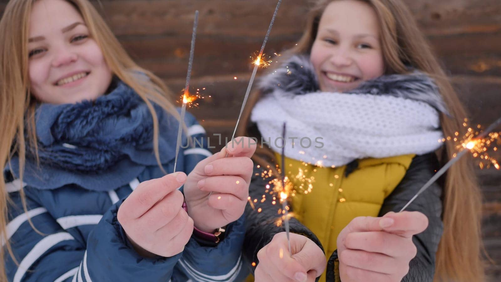 Two young girlfriends with lit Bengal flames in winter by the barn