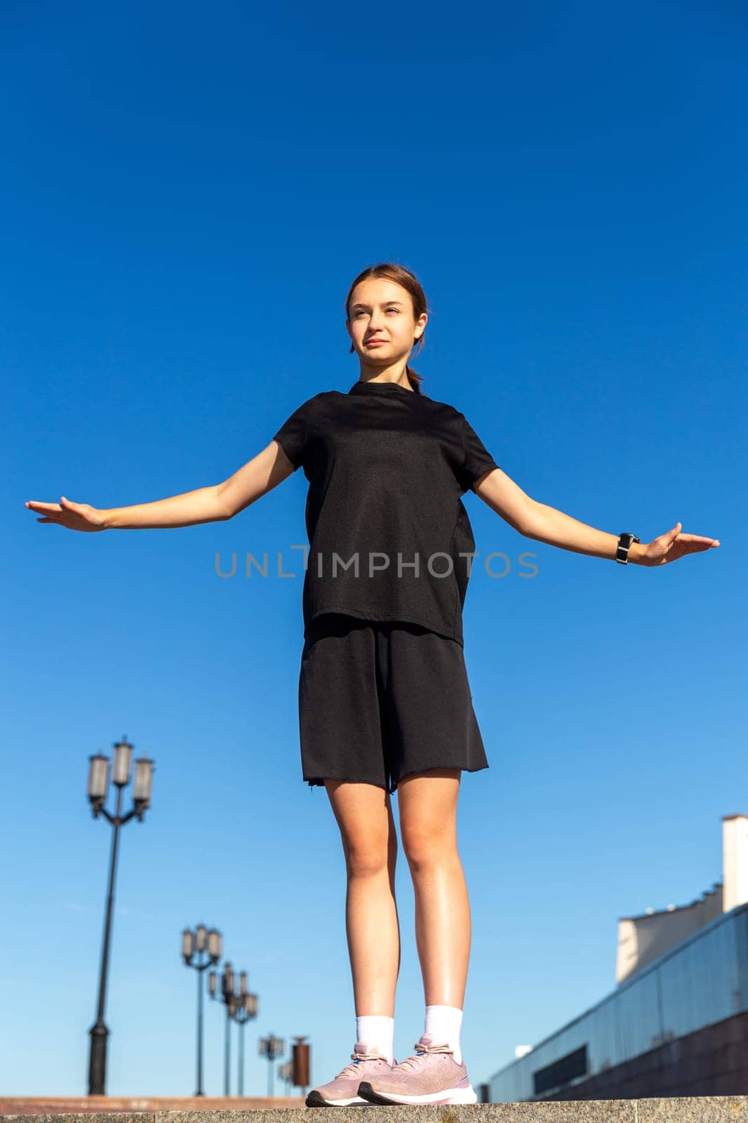 Young, fit and sporty girl in black clothes stretching after the workout in the urban city park. Fitness, sport, urban jogging and healthy lifestyle concept.