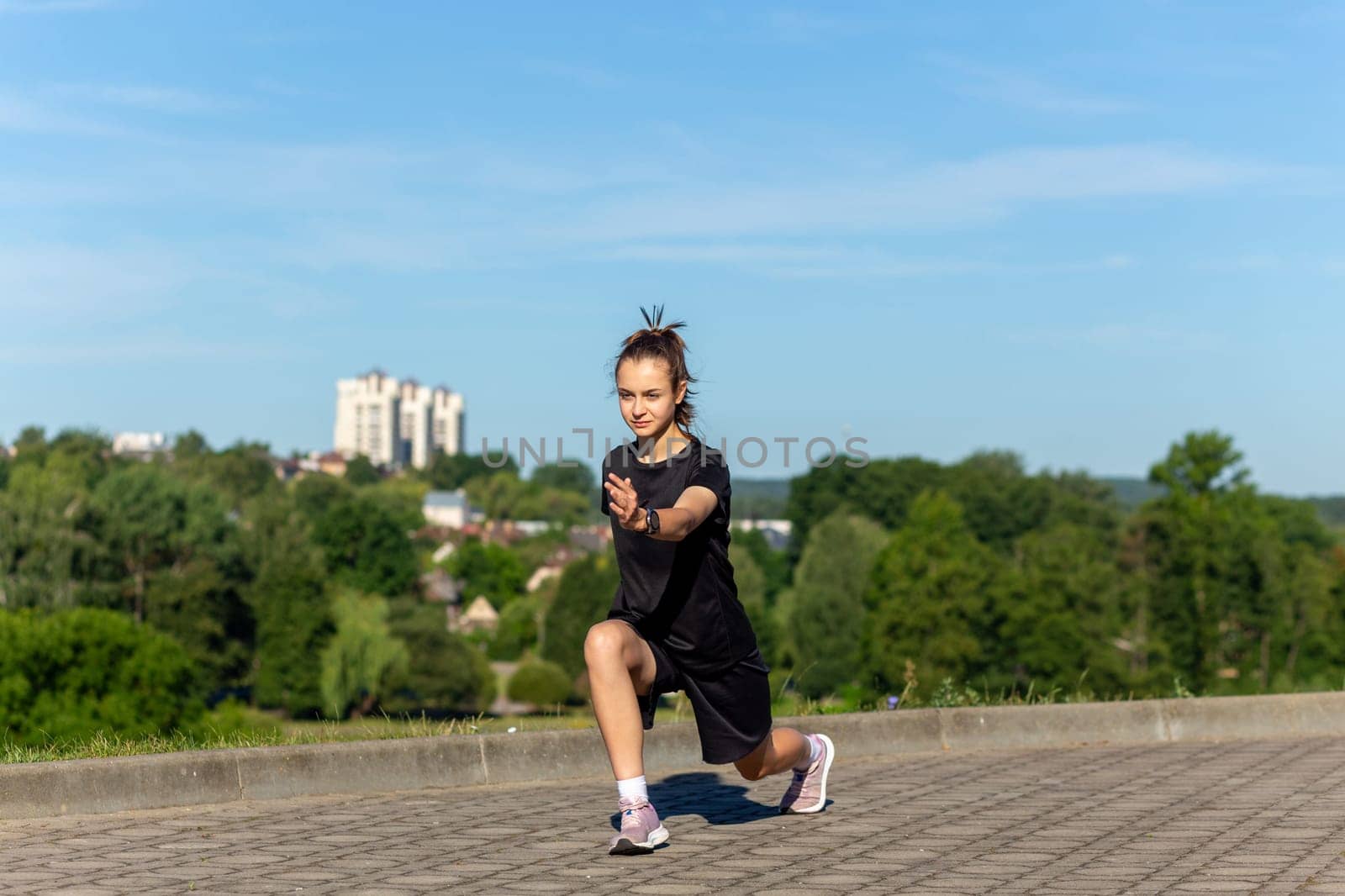Young, fit and sporty girl in black clothes stretching after the workout in the urban city park. by BY-_-BY