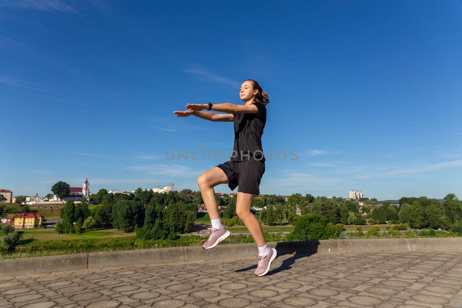 Young, fit and sporty girl in black clothes stretching after the workout in the urban city park. Fitness, sport, urban jogging and healthy lifestyle concept.