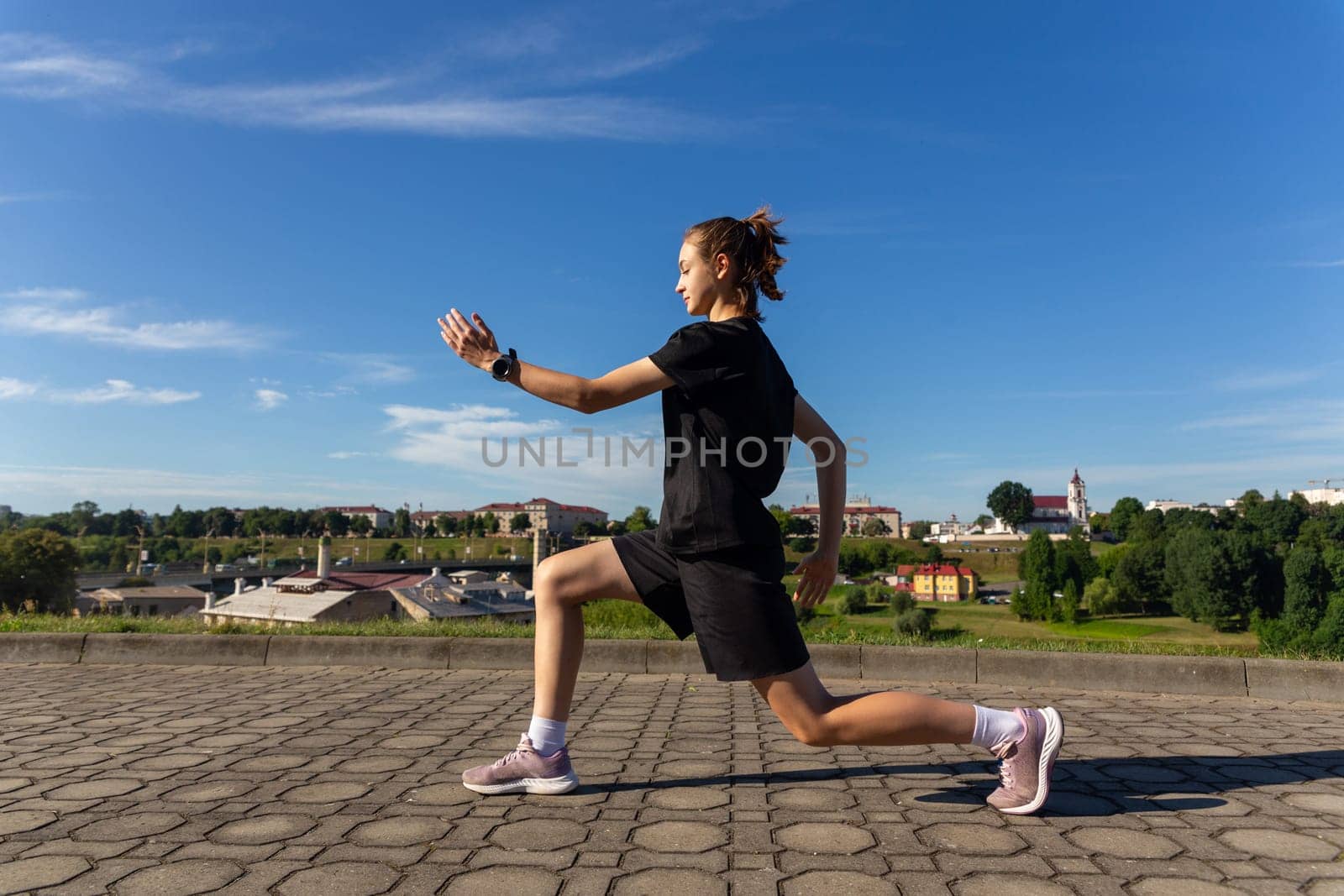 Young, fit and sporty girl in black clothes stretching after the workout in the urban city park. Fitness, sport, urban jogging and healthy lifestyle concept.