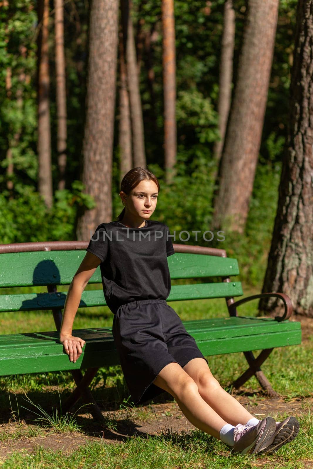 Beautiful young sporty woman in black t-shirt, black shorts and pink trainers warming up exercising triceps dip doing push-ups from bench among trees before running.