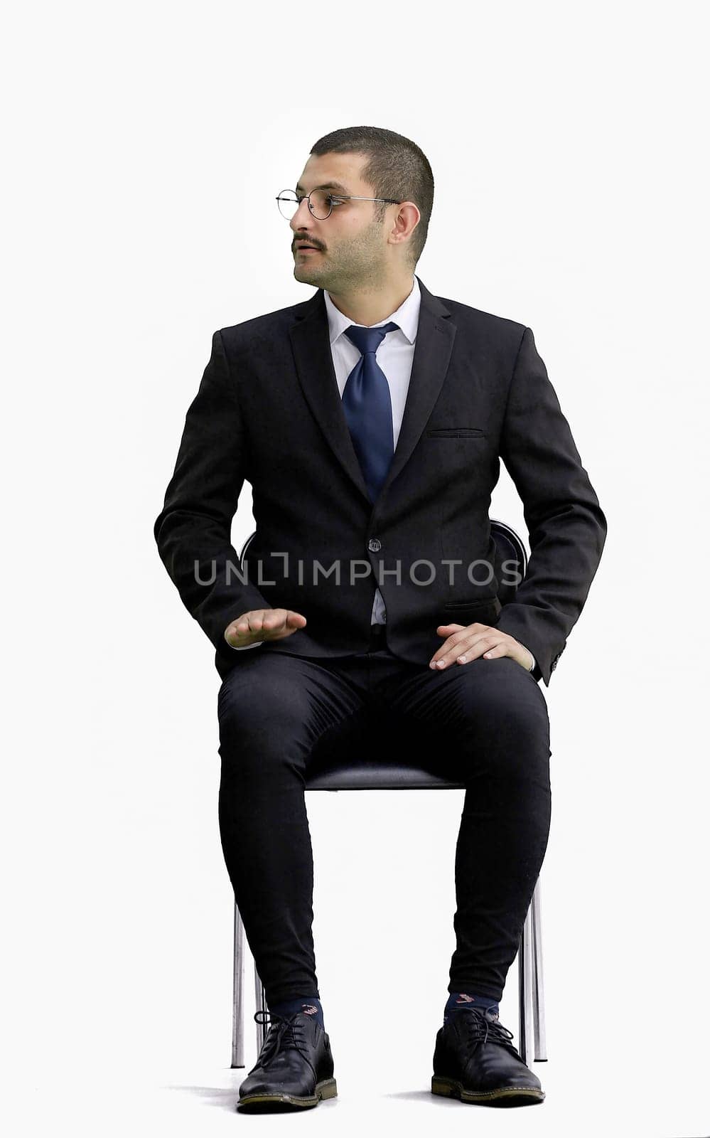 young man in full growth. isolated on a white background sitting on a chair.