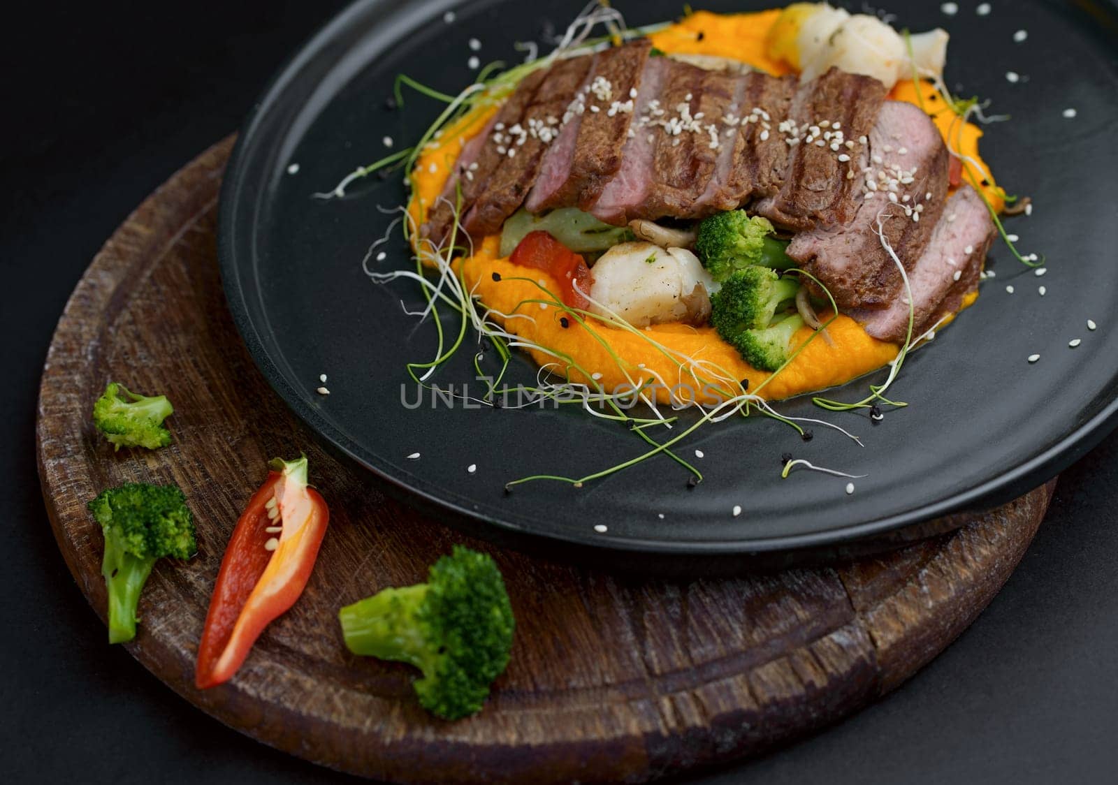 A deliciously appetizing pumpkin puree with chunks of beef meat with spices and herbs in a green plate on a dark table. A hearty lunch in a restaurant. Meat with vegetables in the oven by aprilphoto