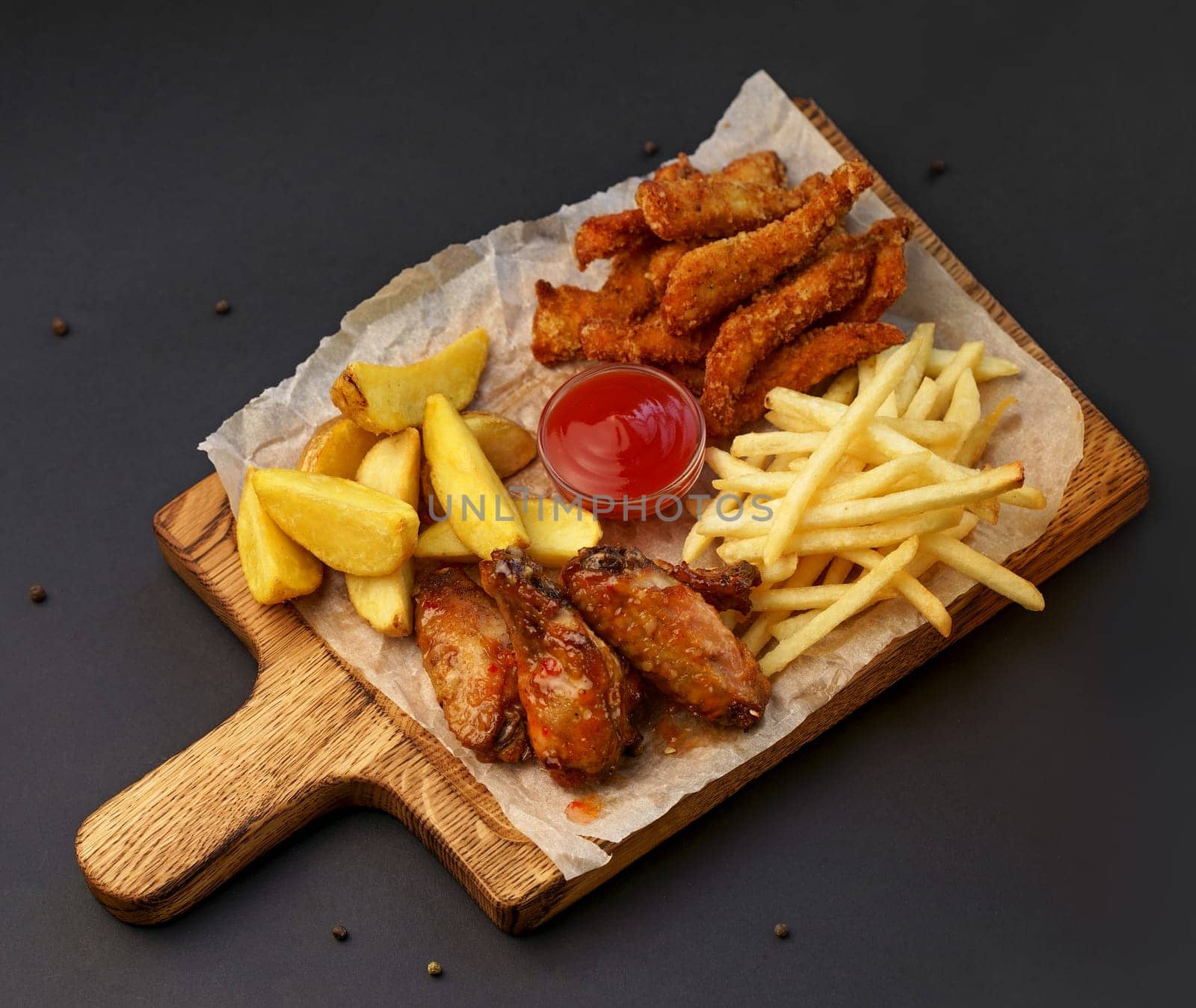 Serving of crispy spicy grilled chicken wings with a chili dip on the side and crinkle cut French Fries or potato chips viewed from above on a dark slate with copy space by aprilphoto