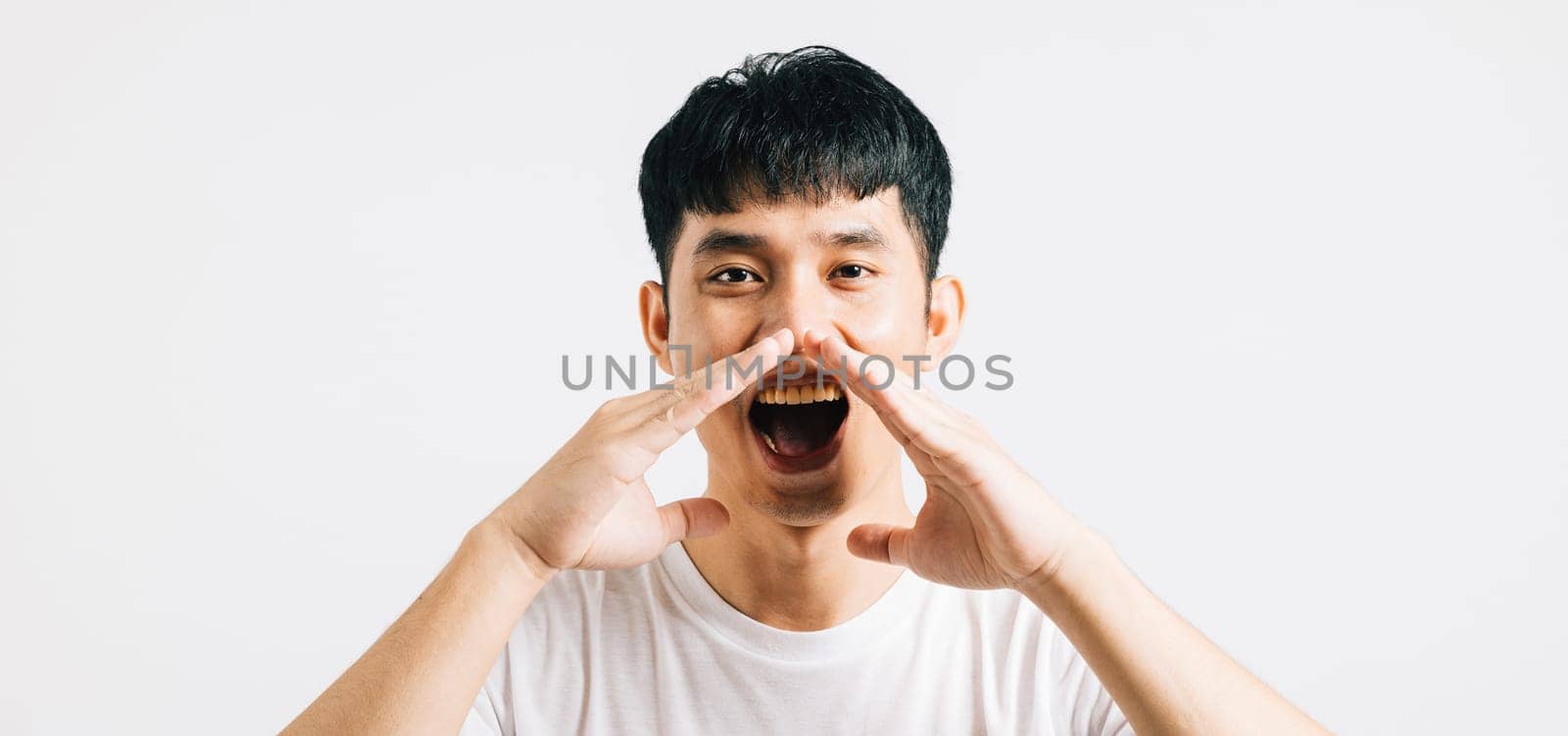 Young Asian man, with a hand on his mouth, shares news or announcements in a studio setting. Isolated on white, ideal for adding your message or copy.