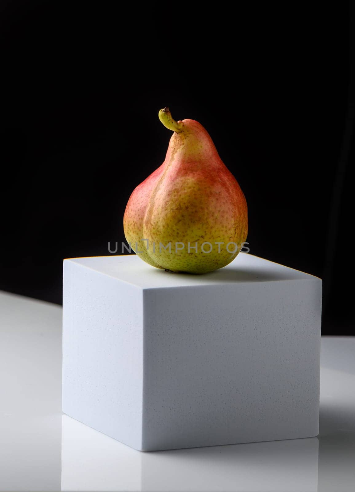 fresh pear on white cube on black background