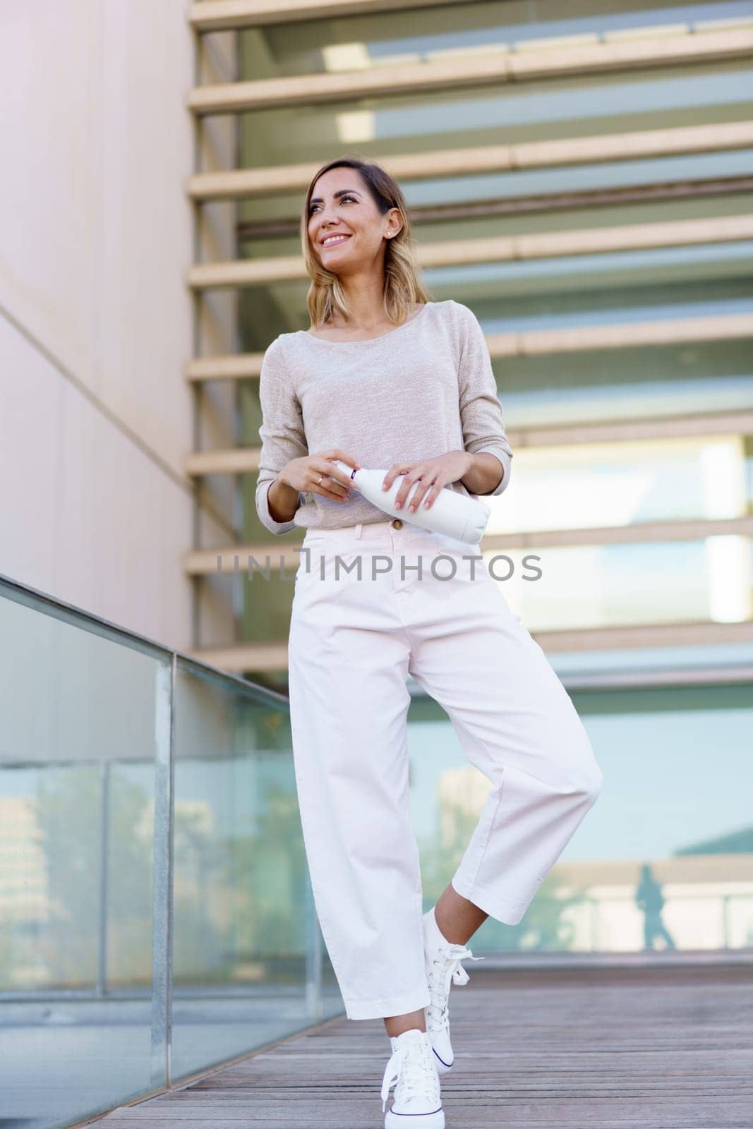 Middle aged woman wearing casual clothes carrying an eco-friendly ecological metal water bottle. Caucasian female in urban background.
