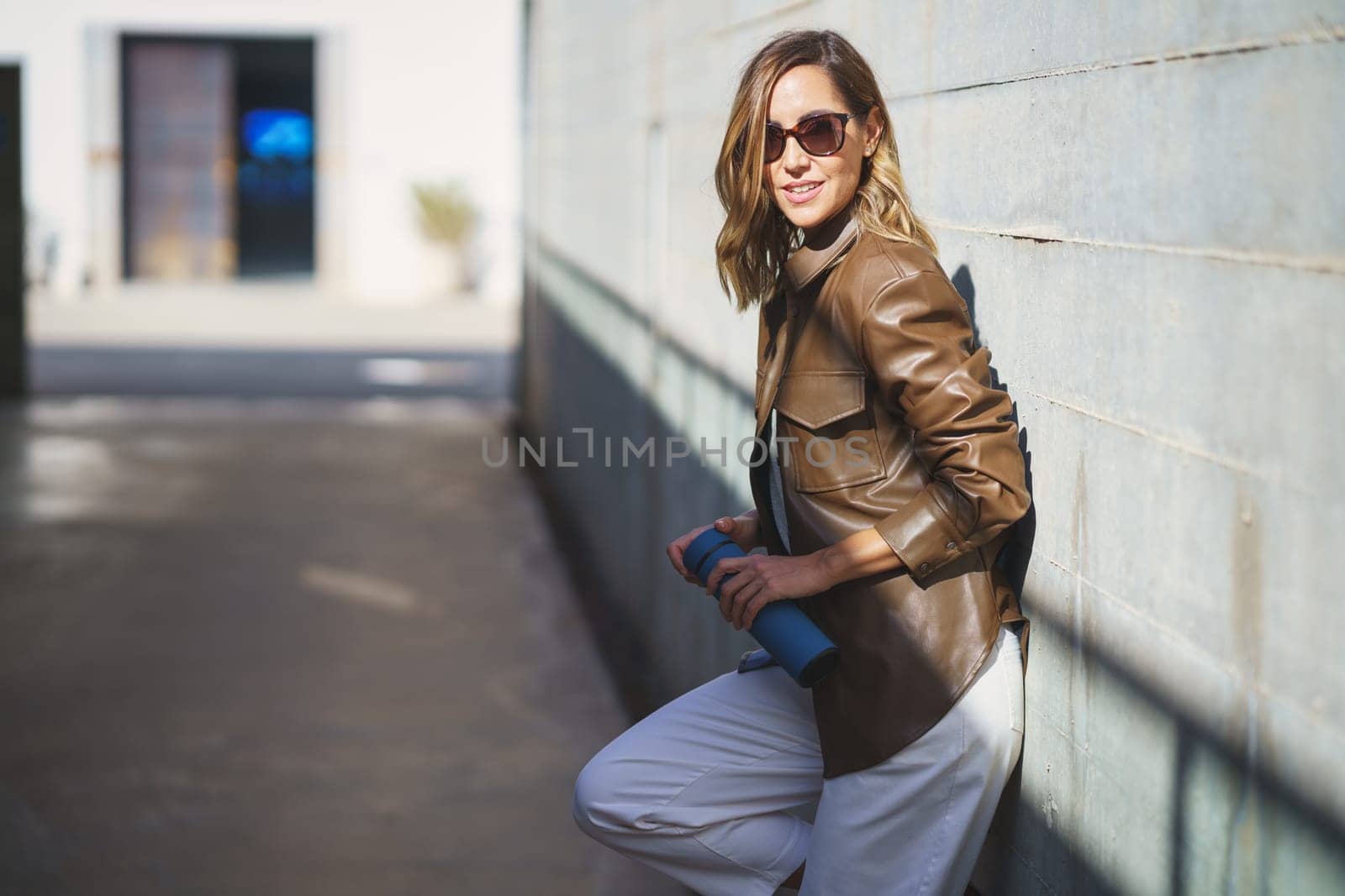 Middle aged woman with sunglasses taken a coffee break carrying an eco-friendly a thermos for coffee. Caucasian female in urban background.