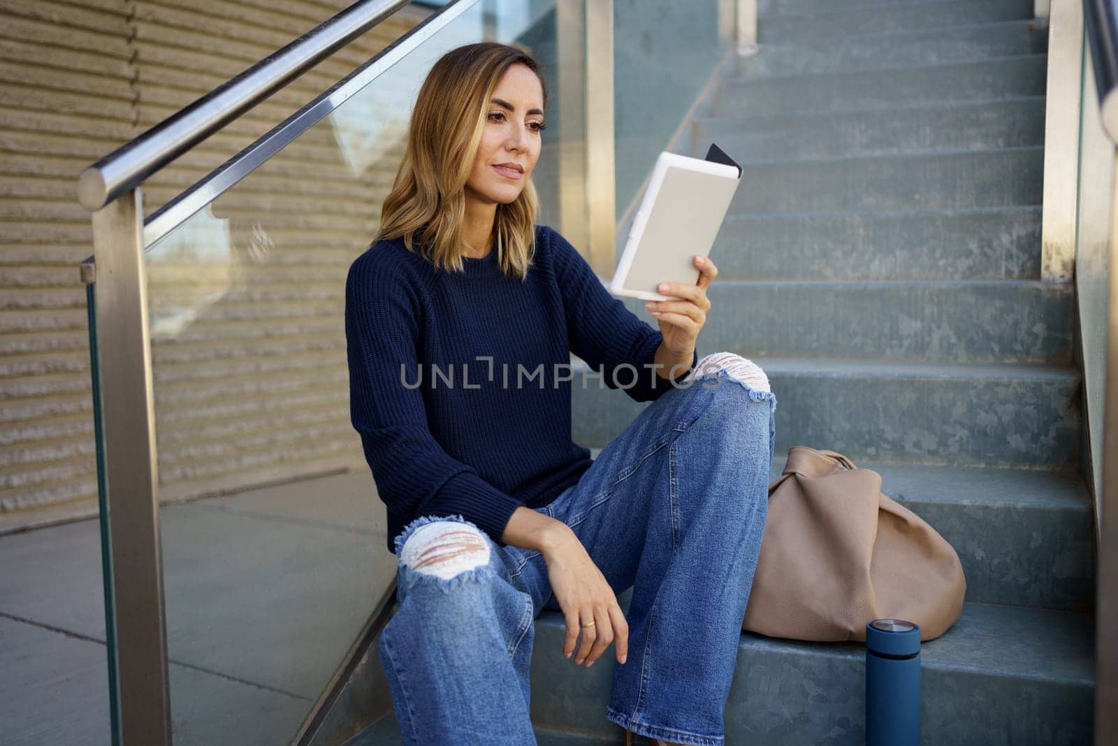 Middle-aged woman reading with her e-book on a coffee break near her office. Caucasian female wearing casual clothes.