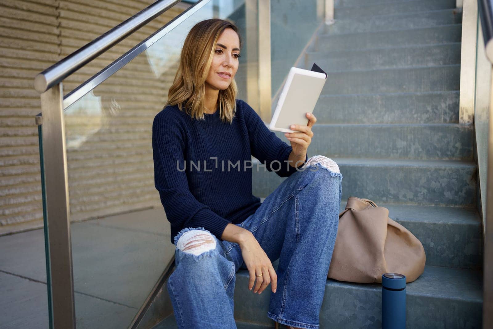 Middle-aged woman reading with her e-book on a coffee break near her office. by javiindy