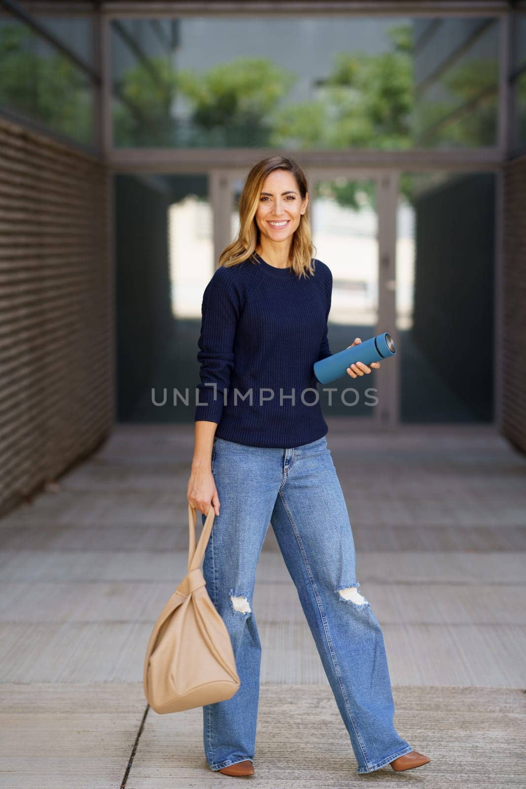 Middle-aged woman carrying a bag and an eco-friendly ecological metal thermos for coffee. Caucasian female in urban background.