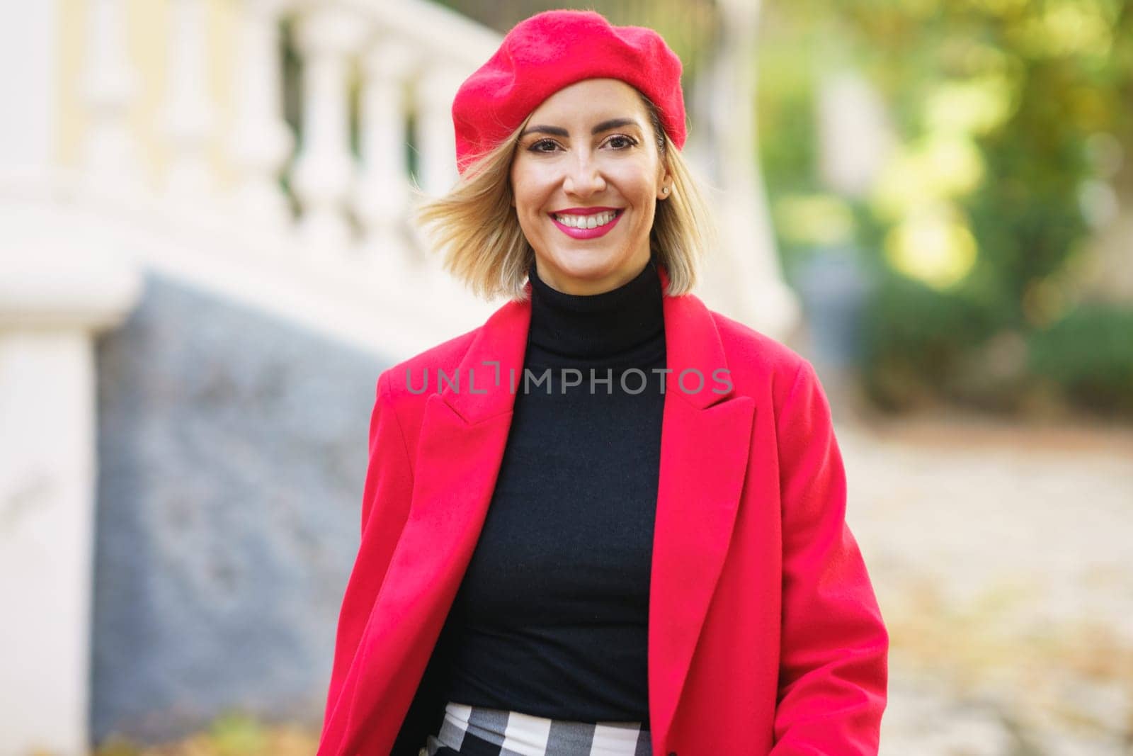 Positive female in trendy red outfit looking at camera with flying hair while strolling in street of city against blurred background