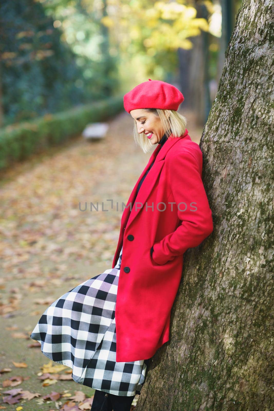 Smiling woman standing near tree in park by javiindy