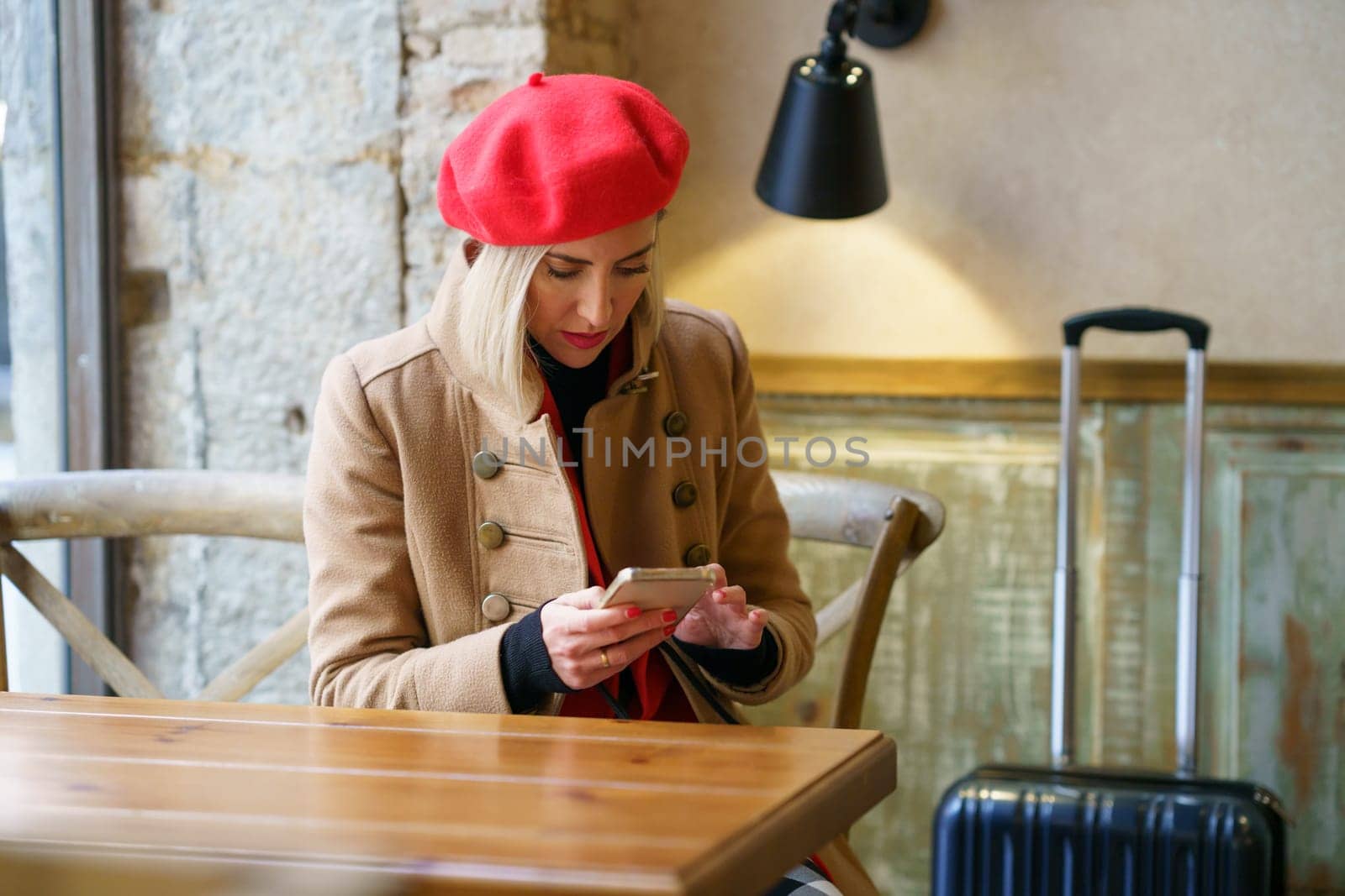 Woman travelling for work, waiting for a coffee in a cafe bar to take a break, while checking her smartphone. Female commuter taking a break.