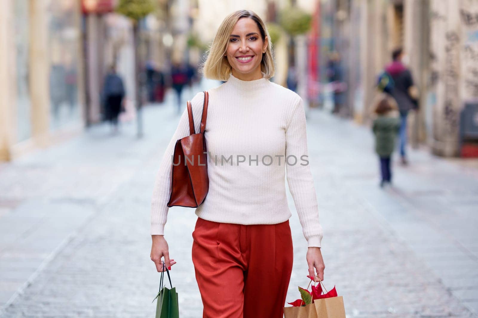 Cheerful woman with shopping bags on street by javiindy