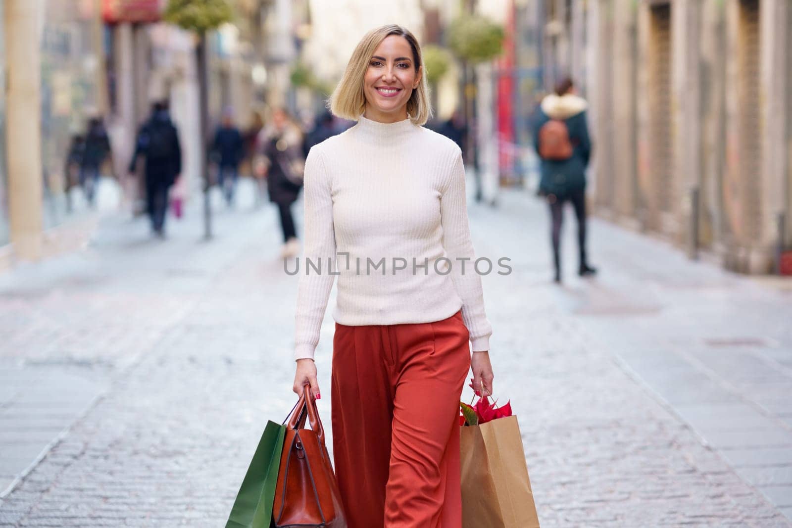 Smiling woman carrying shopping bags on paved street by javiindy