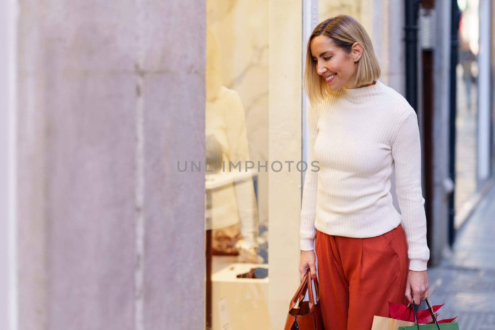 Smiling woman looking through showcase of store by javiindy