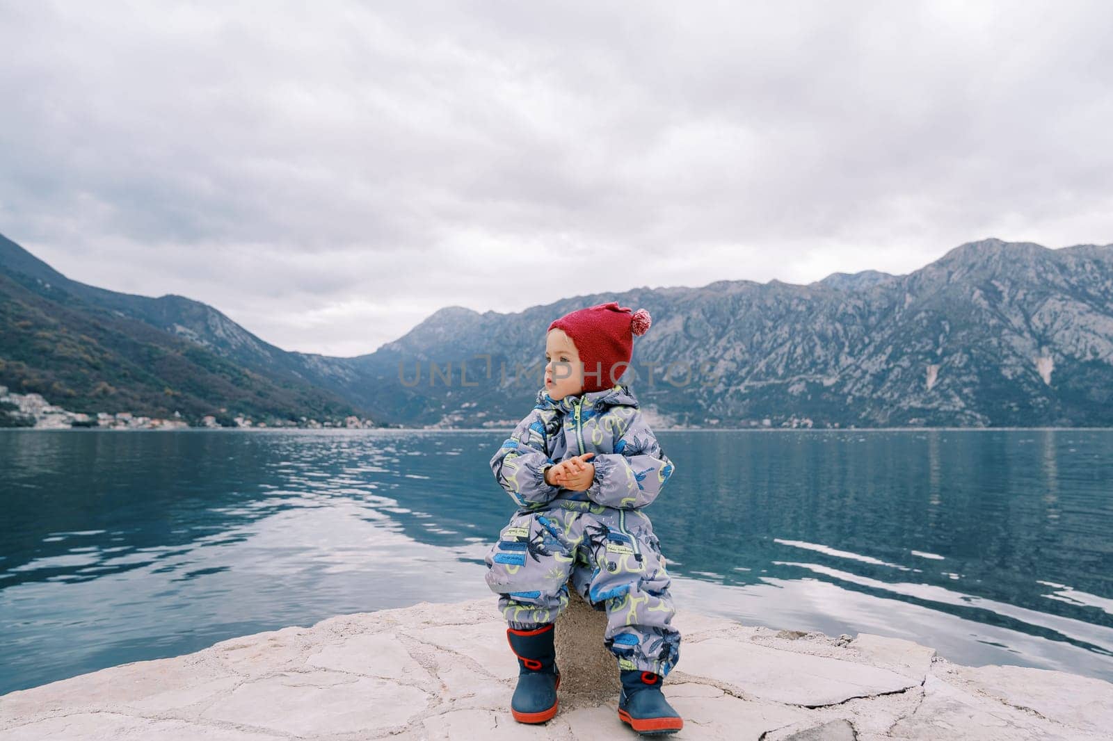 Little girl sits on a bollard on the pier and looks away. High quality photo