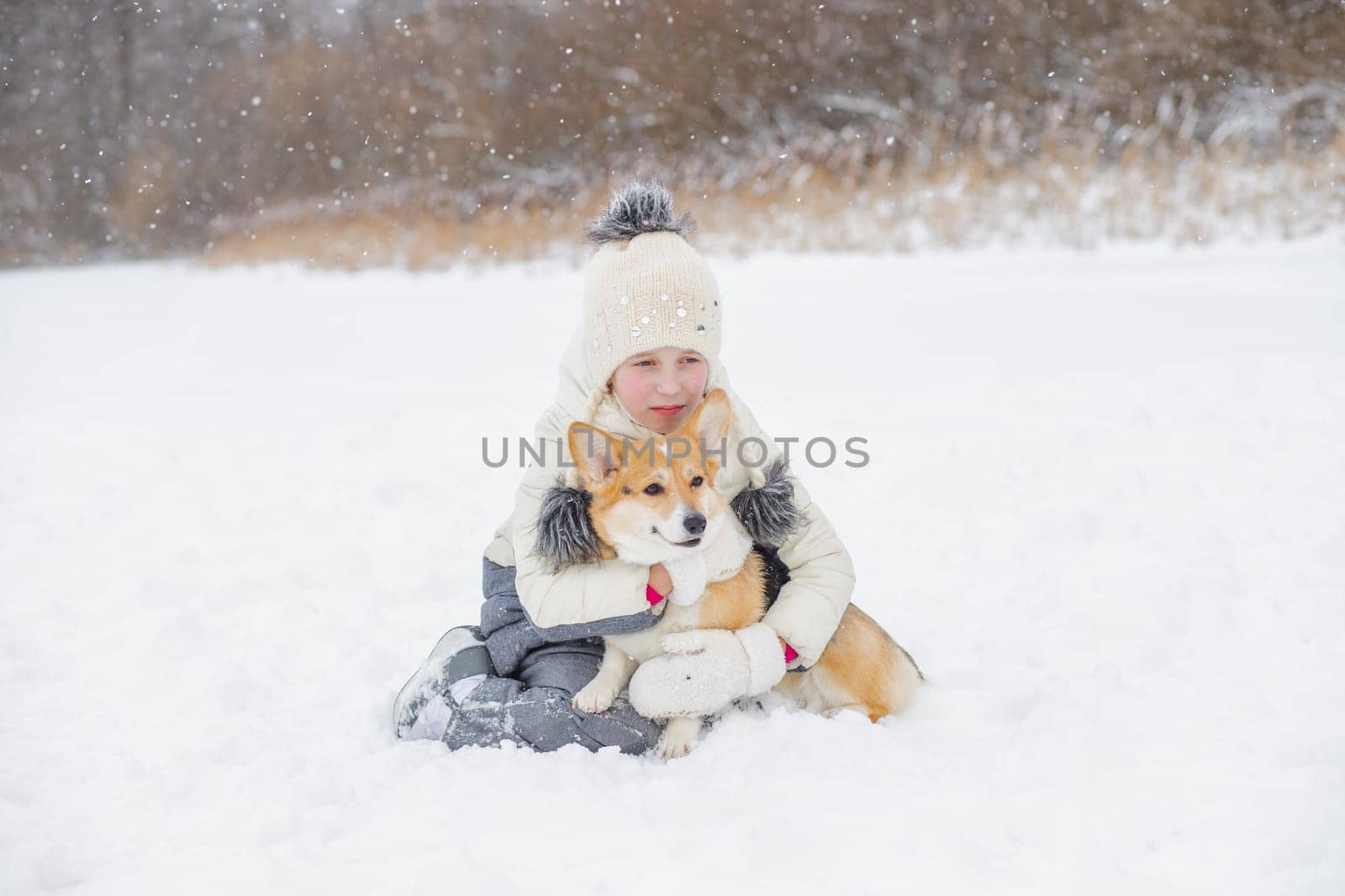 happy child having fun in snowy winter park with Corgi baby dog.Walking the dog in the park in winter. girl plays with corgi. copy space by YuliaYaspe1979