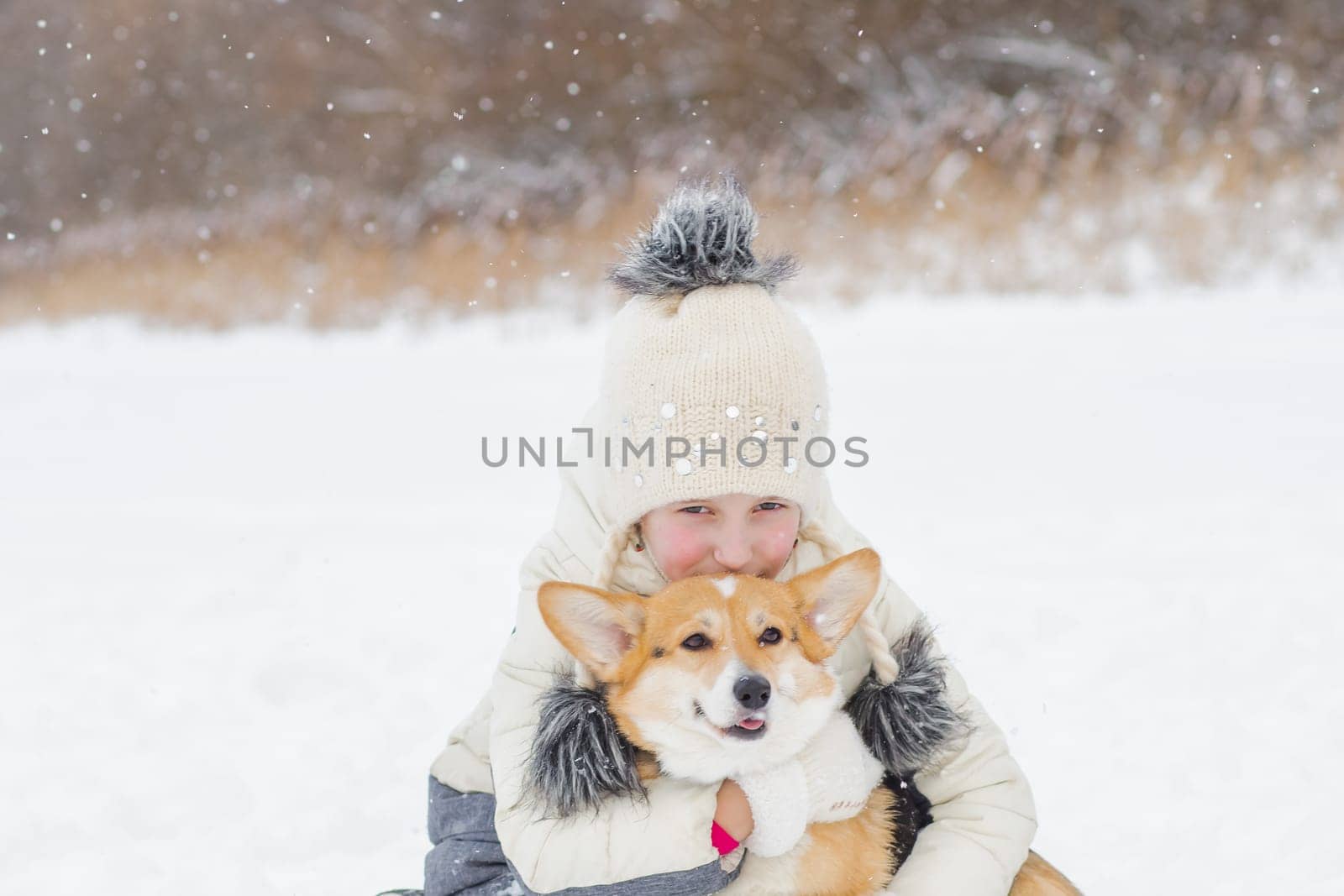 A Young happy woman having fun in snowy winter park with Corgi baby dog