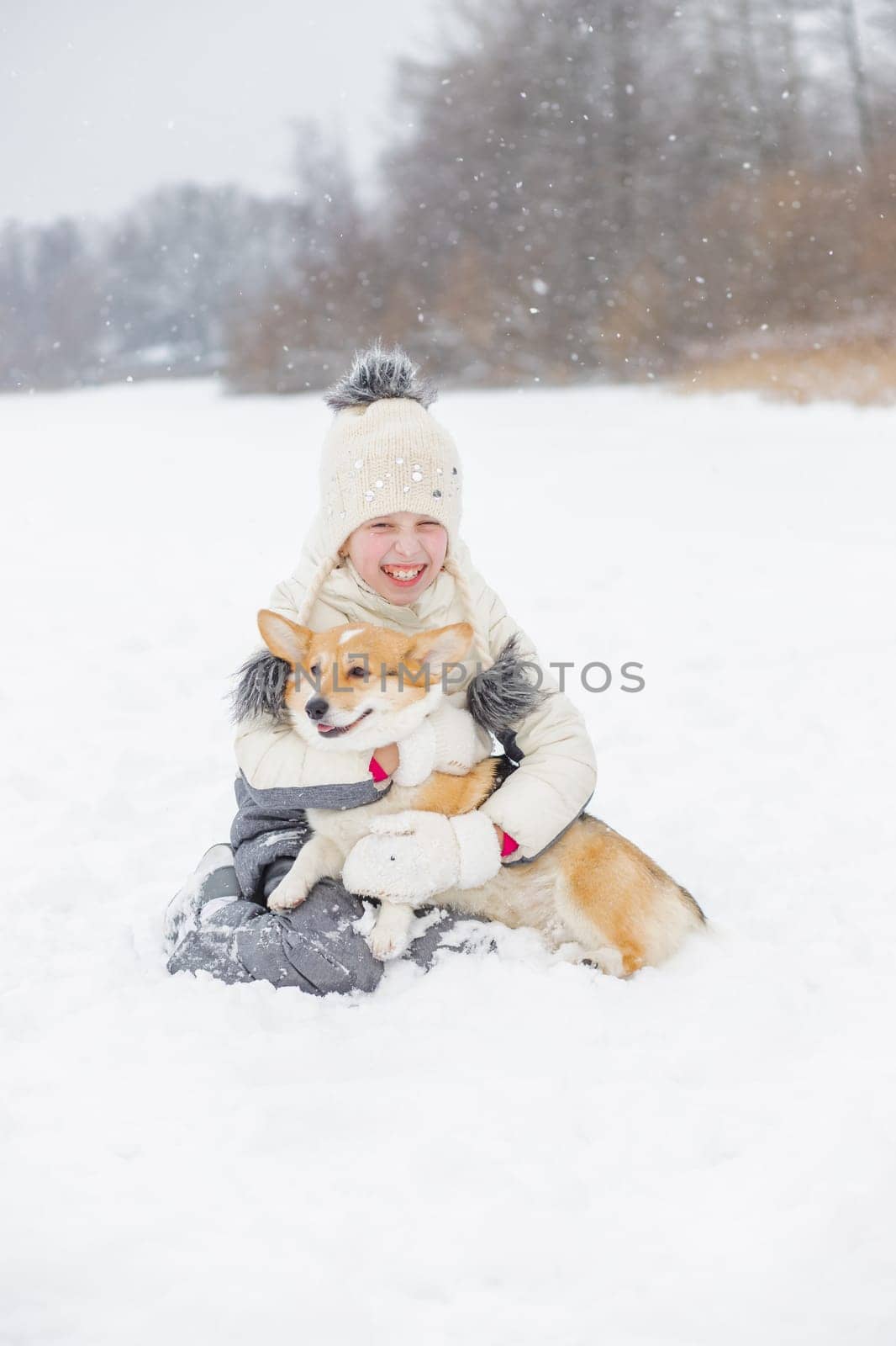 A Young happy woman having fun in snowy winter park with Corgi baby dog