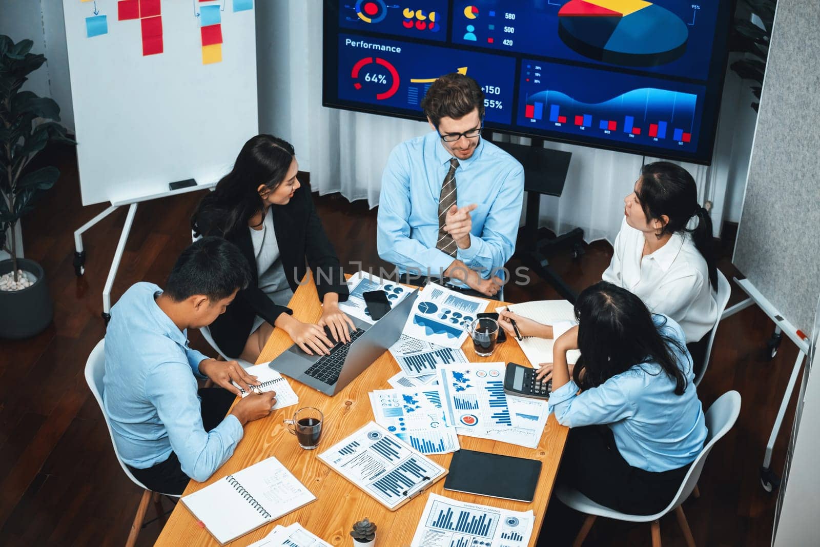 Wide top view of diverse group of business analyst team analyzing financial data report paper on meeting table. Chart and graph dashboard by business intelligence analysis. Meticulous