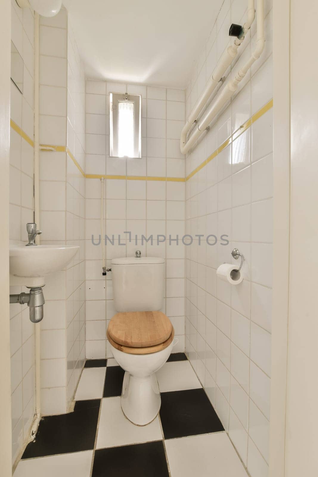 a small bathroom with black and white tiles on the floor, including a wooden seat in the toilet is next to the sink