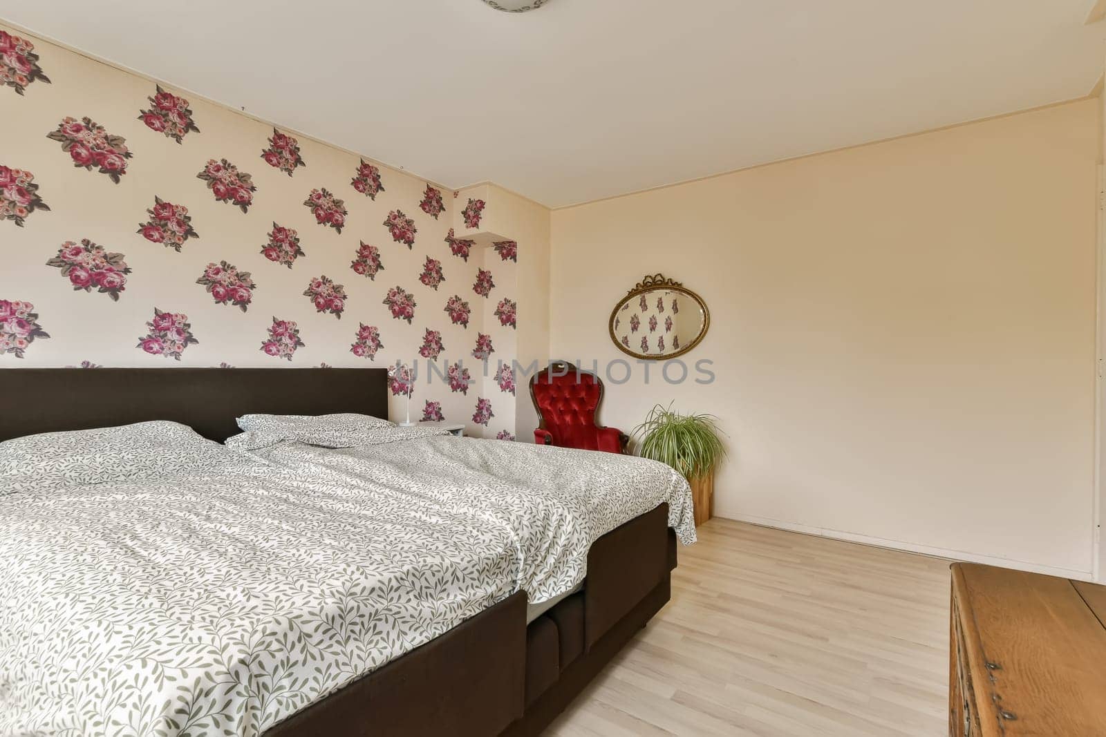 a bedroom with floral wallpaper on the walls and wood flooring in front of the bed, there is a mirror hanging above