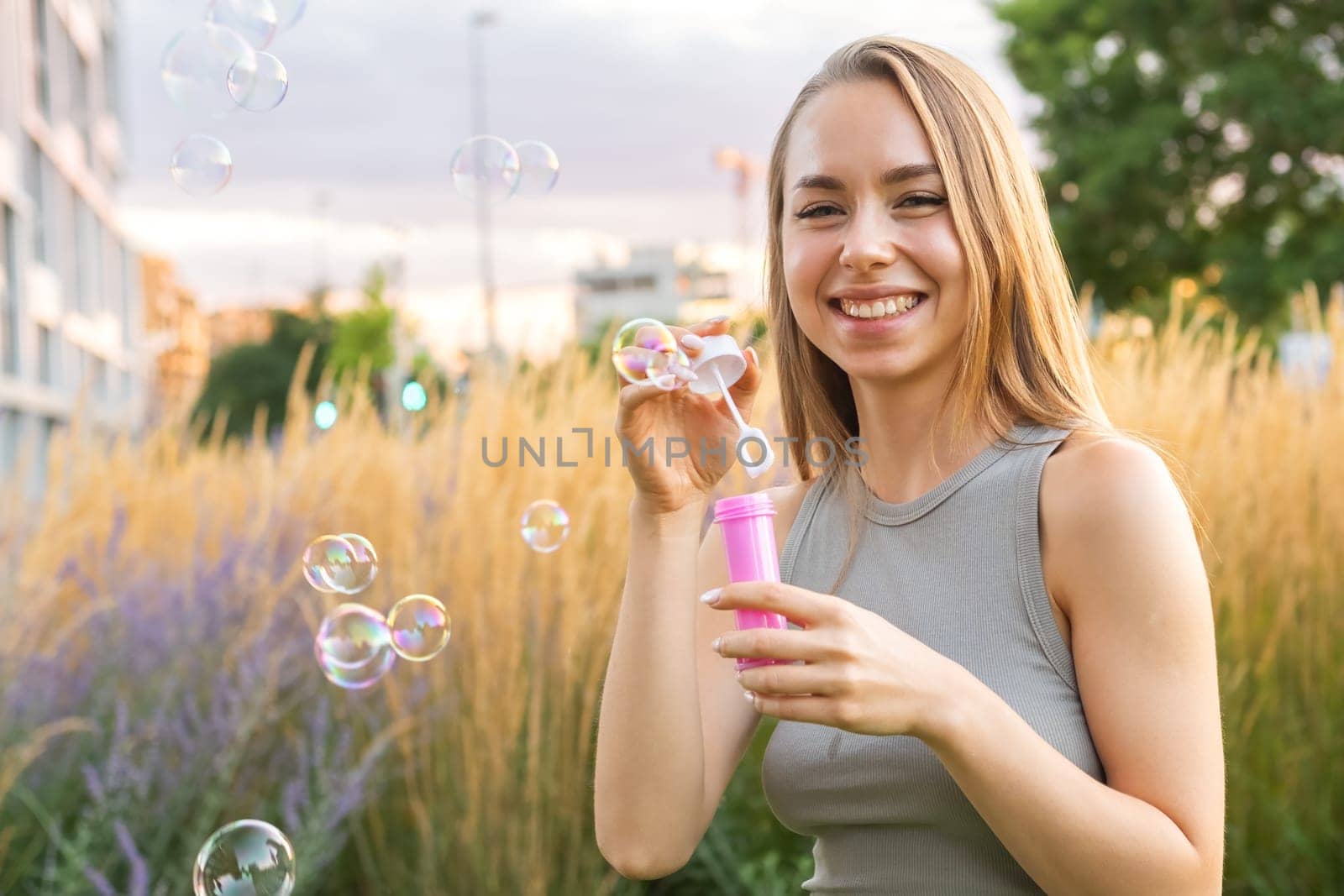 A joyous lady with long, flowing hair creates soap bubbles and smiles in the park.