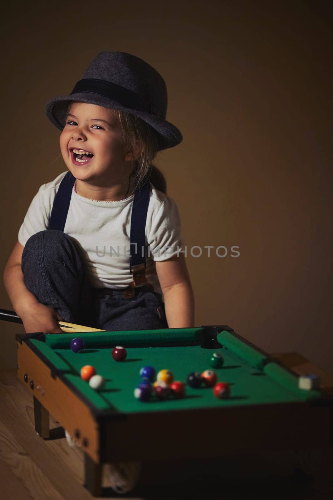 Charming child in retro clothes playing toy billiards.