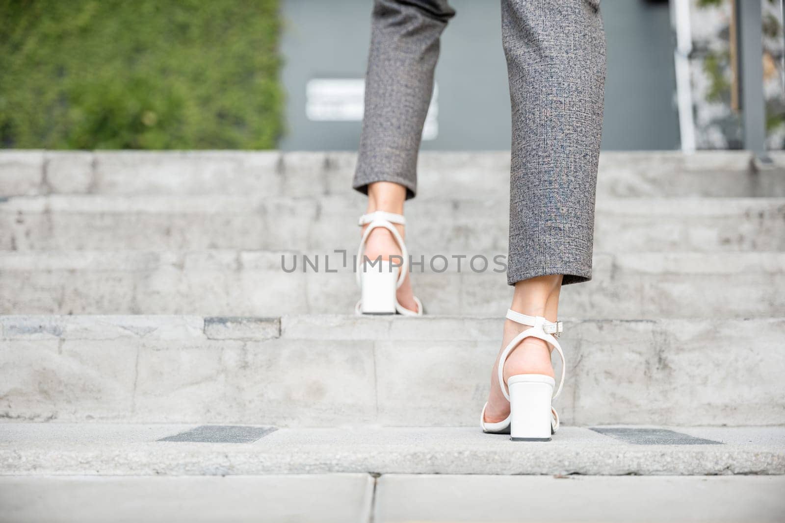 In bustling city a determined businesswoman legs in motion are captured on office stairway. Her black shoe signifies constant pursuit of success, progress, and achievement in dynamic business setting. by Sorapop