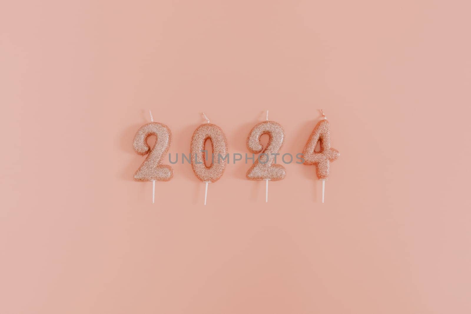 Shiny candles with the number 2024 lie in a row in the center on a pink background, flat lay close-up.