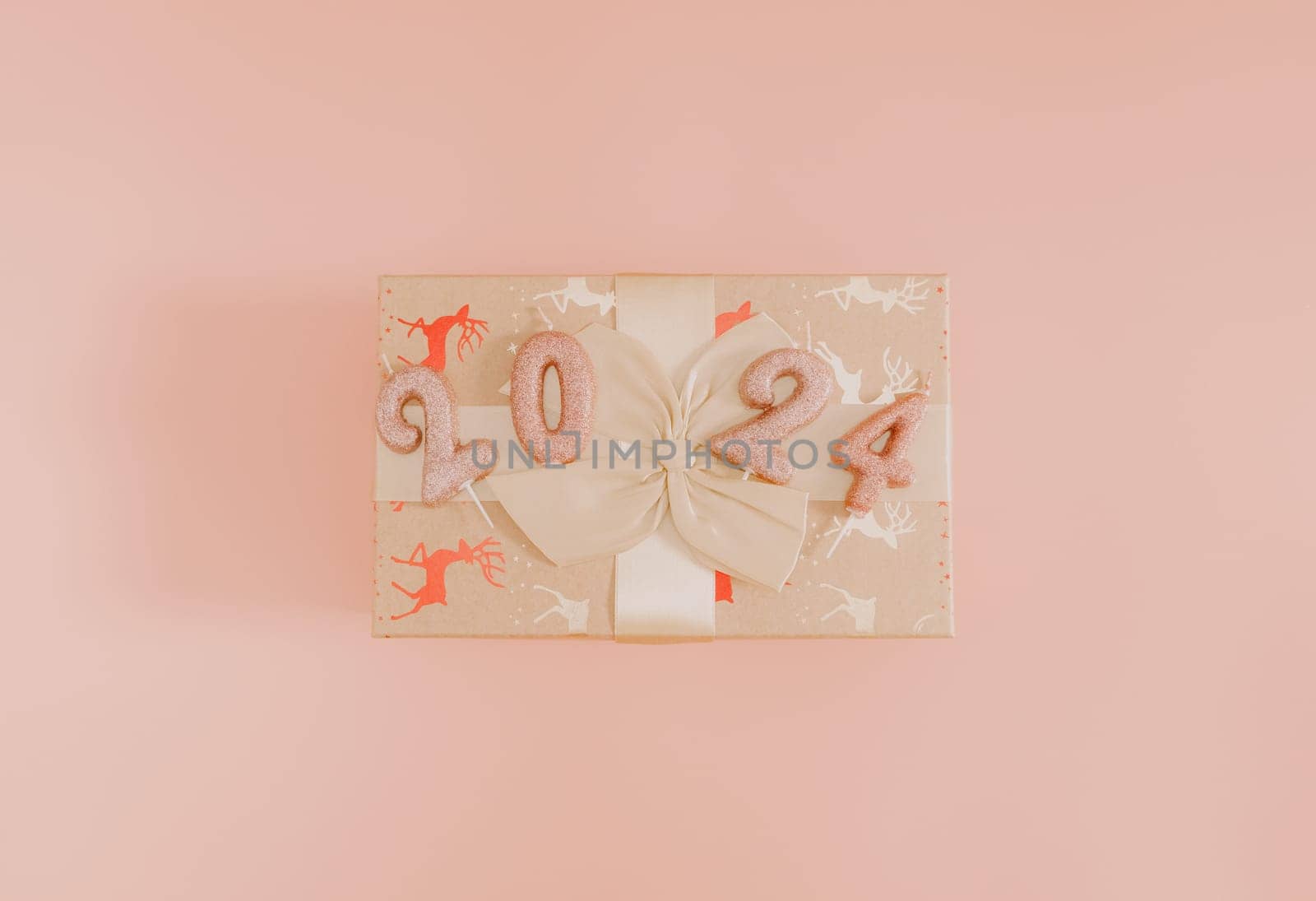 Shiny candles with the number 2024 on a gift box tied with a bow lie in the center on a pink background, flat lay close-up.