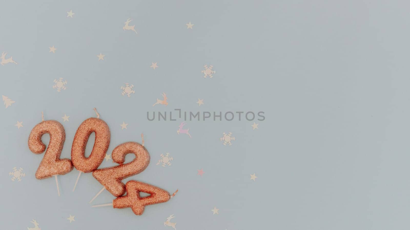 Shiny light brown candles number 2024 lie with white shiny holiday confetti lie on the left on a pastel blue background with copy space on the right, flat lay close-up.