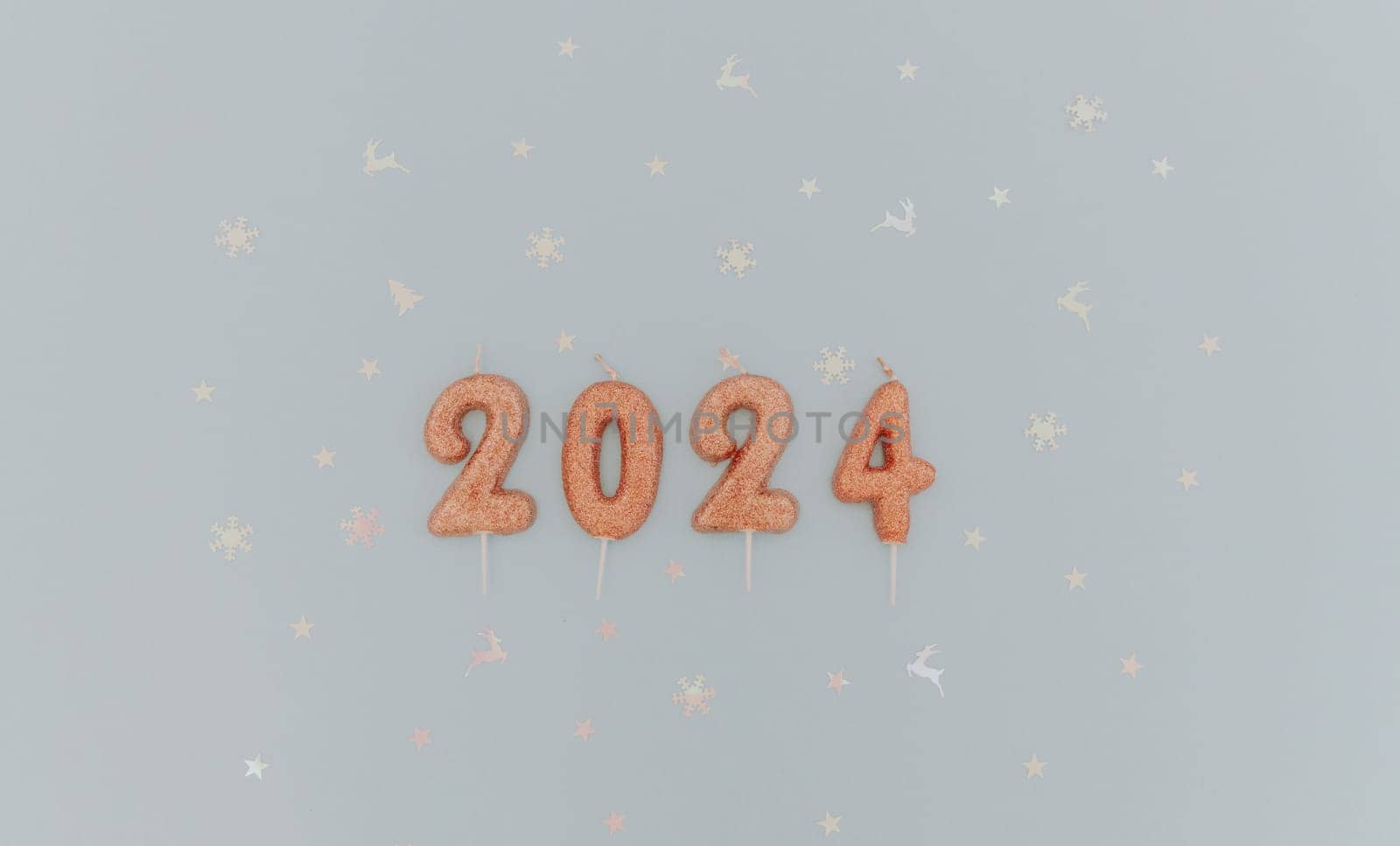 Shiny light brown candles number 2024 lie with white shiny festive confetti lie in the center on a pastel blue background with copy space on the sides, flat lay close-up.