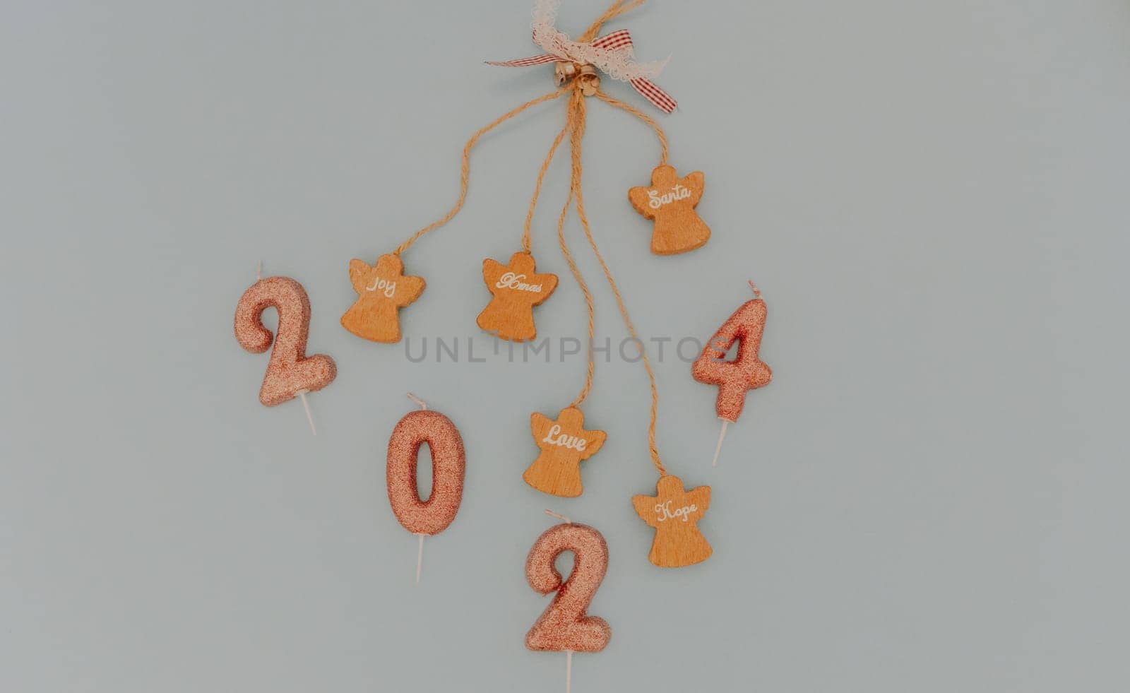 One holiday decoration with wooden angels, motivational words hanging on a blown string and light brown glitter candles number 2024 lies in the center on a pastel blue background, flat lay close-up.