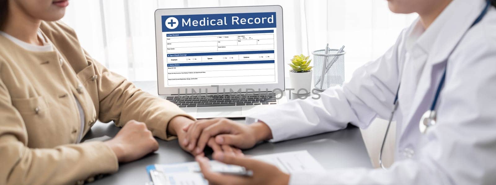 Doctor show medical diagnosis report on laptop and providing compassionate healthcare consultation while being supportive and holding young patient hand in doctor clinic office. Neoteric