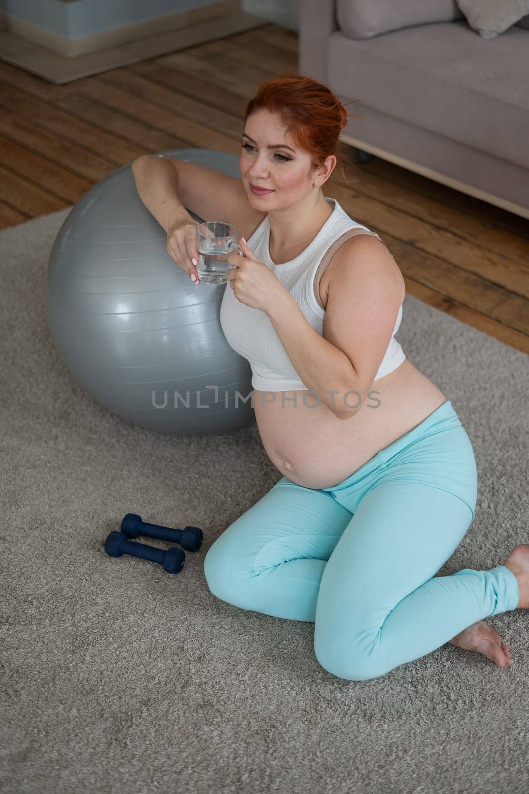 Pregnant woman drinks water after workout on fitness ball