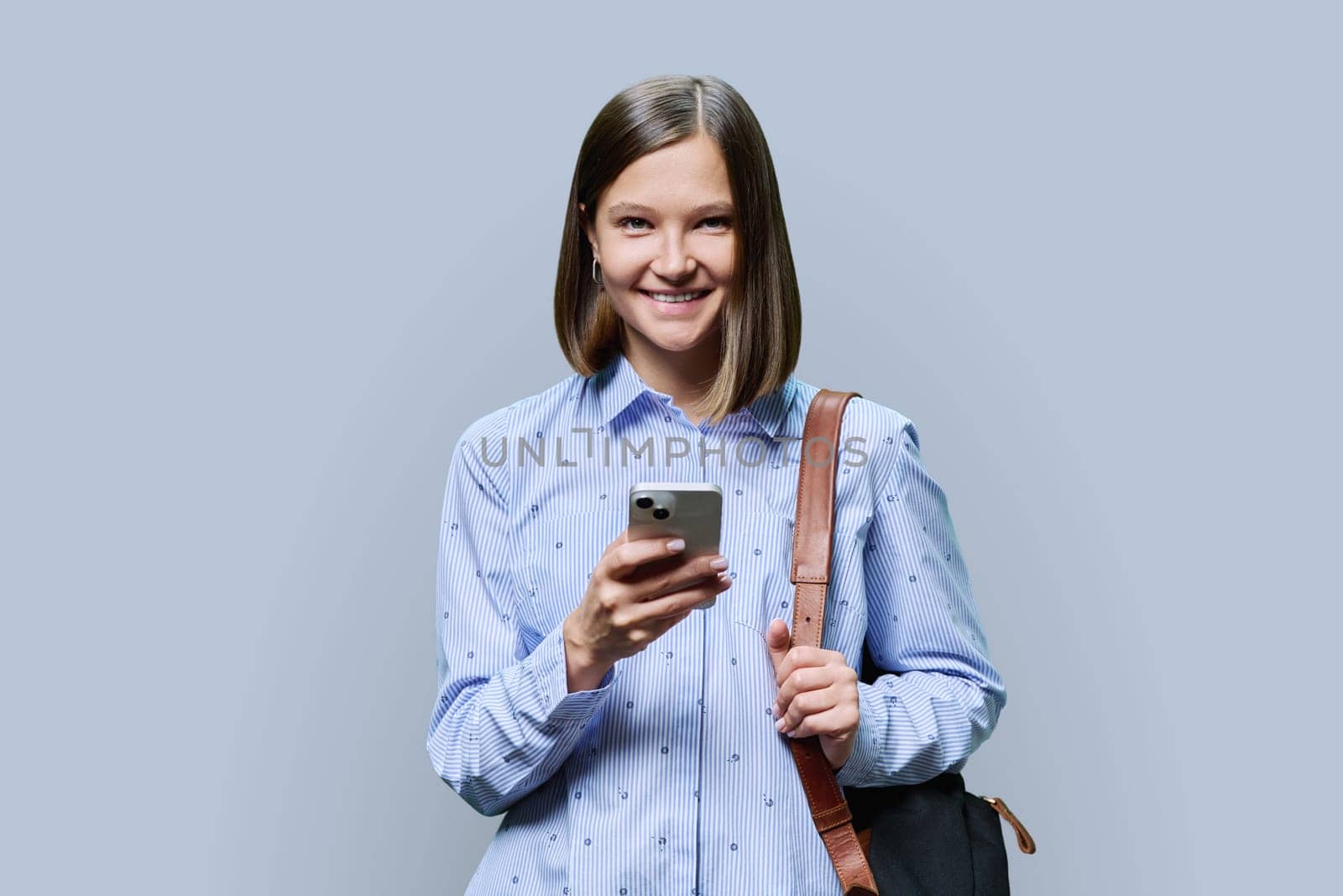 Young woman student with smartphone backpack on grey studio background by VH-studio