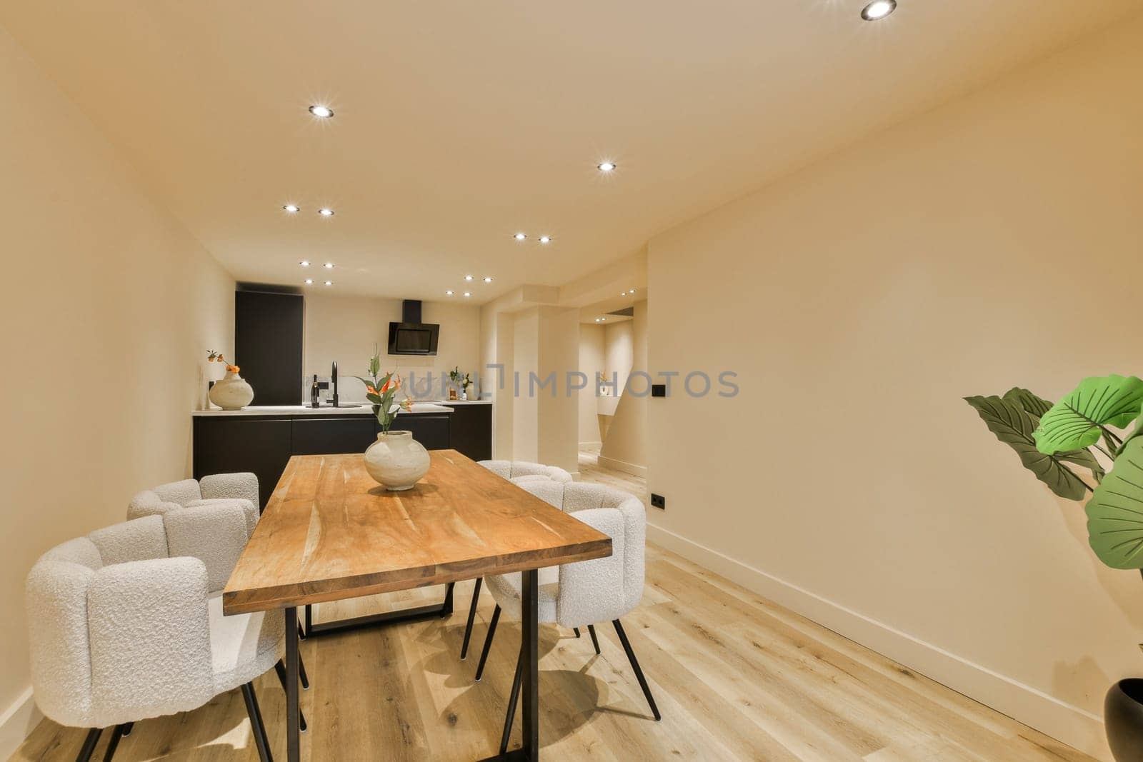 a dining room with white chairs and a wooden table in the center of the room is an open kitchen area