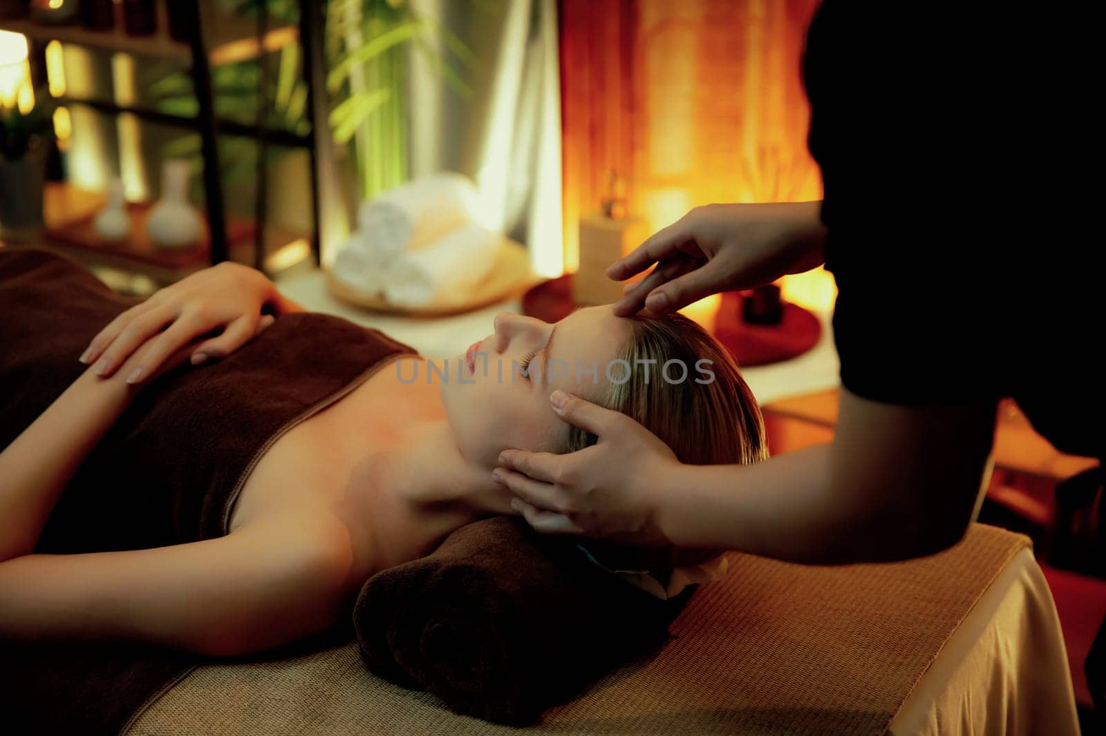 Caucasian woman enjoying relaxing anti-stress head massage and pampering facial beauty skin recreation leisure in warm candle lighting ambient salon spa in luxury resort or hotel. Quiescent