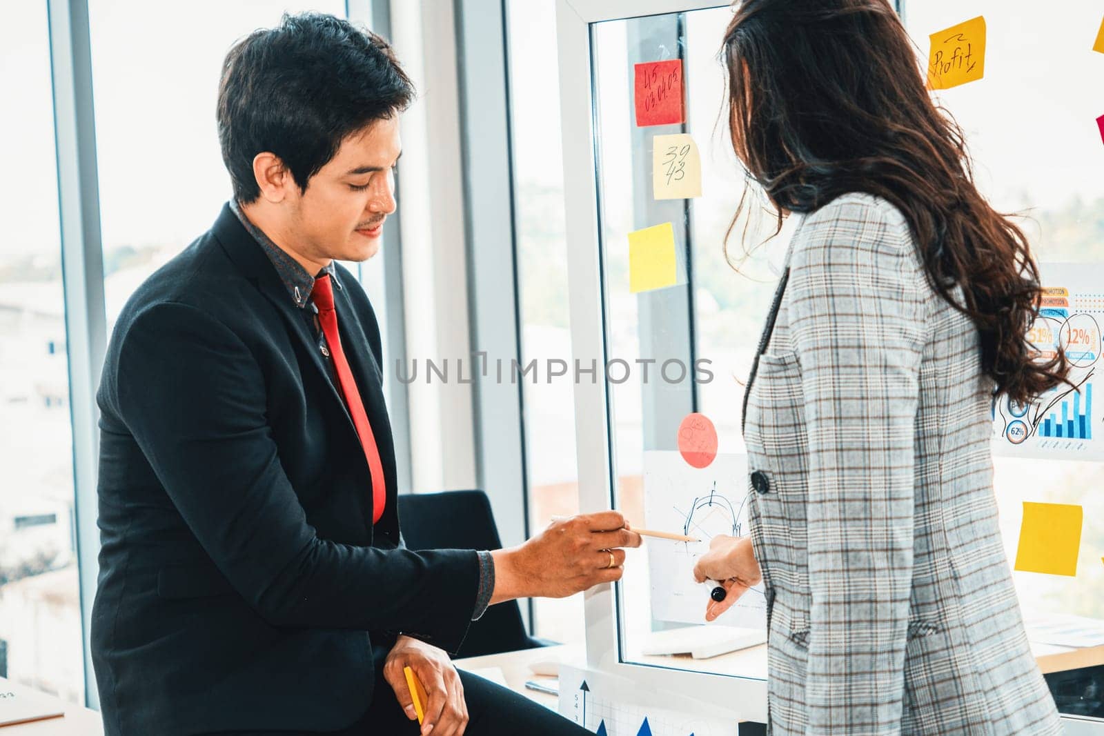 Business people work on project planning board in office and having conversation with coworker friend to analyze project development . They use sticky notes posted on glass to make it organized. Jivy